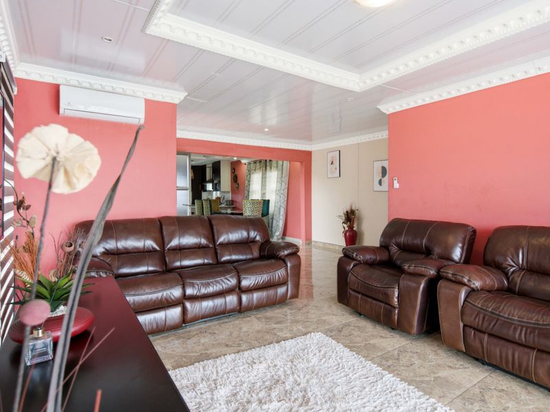 A spacious living room featuring tiled flooring, decorative ceiling cornices, and a wall-mounted air conditioning unit, with an open-plan flow to the adjacent kitchen area.
