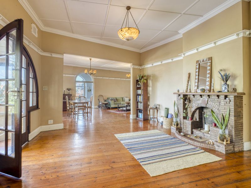 Spacious living room featuring original hardwood floors, a classic brick fireplace, and elegant coffered ceilings, flowing into an adjacent dining area.