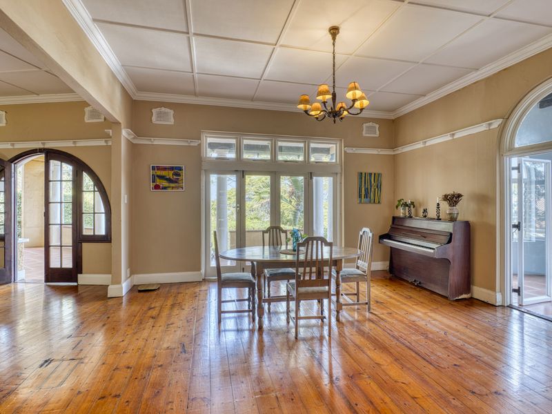 Spacious dining room featuring polished hardwood floors, classic coffered ceilings, and multiple sets of arched french doors leading to outdoor areas.