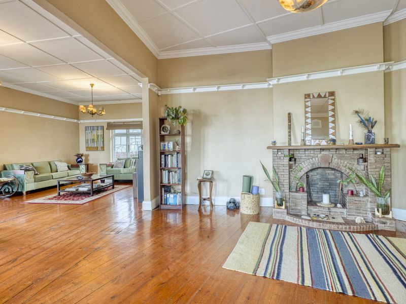 Spacious living room featuring original timber flooring, a classic brick fireplace, and high ceilings with decorative coving.