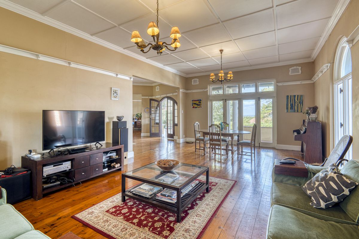 Spacious living room featuring polished hardwood floors, a coffered ceiling, and classic arched windows with access to an outdoor area.