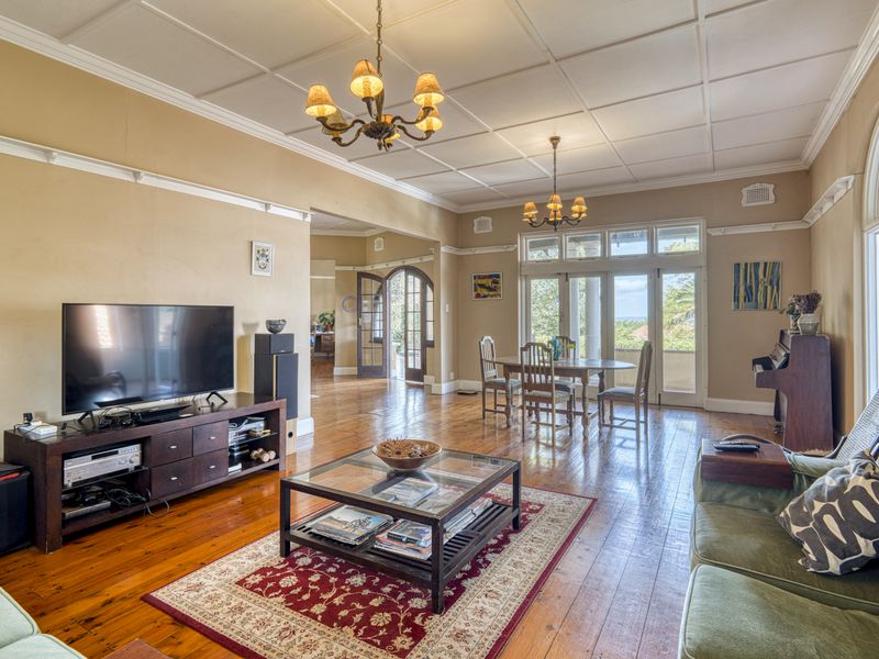 Spacious living room featuring polished hardwood floors, a coffered ceiling, and classic arched windows with access to an outdoor area.