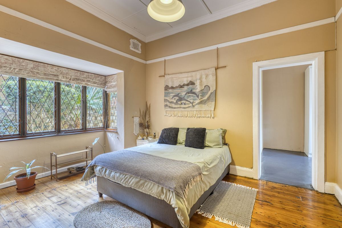 A bedroom featuring original timber flooring, a leaded glass bay window, and classic architectural details including a picture rail and ceiling rose.