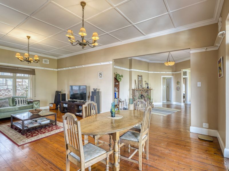 Spacious open-plan living and dining area featuring original hardwood flooring, a classic coffered ceiling, and a charming brick fireplace.