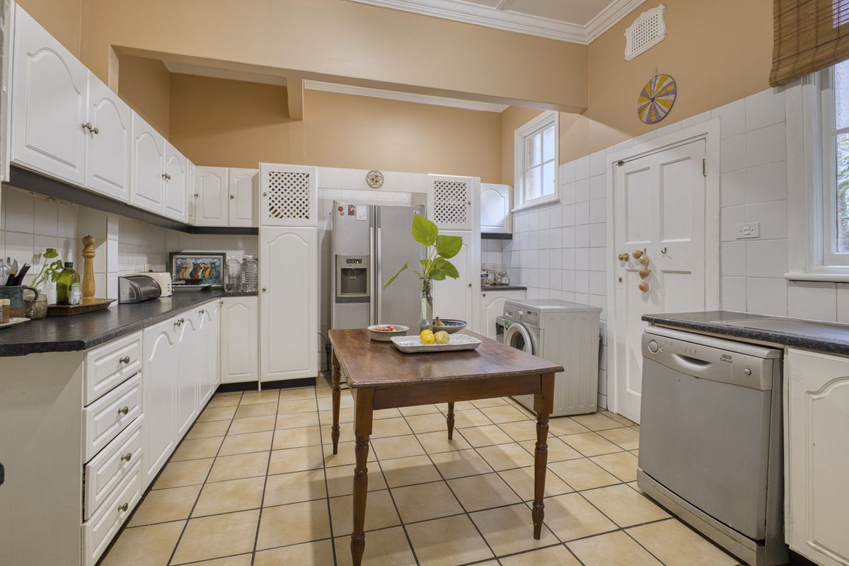 A functional kitchen featuring white cabinetry, tiled splashbacks, tiled flooring, and integrated appliance spaces, offering a classic layout with potential for modern updates.