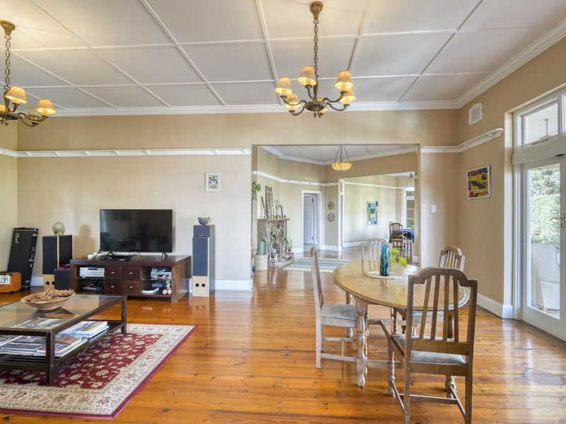 Spacious open-plan living and dining area featuring polished hardwood floors, classic coffered ceilings, and direct access to the outdoor patio through french doors.