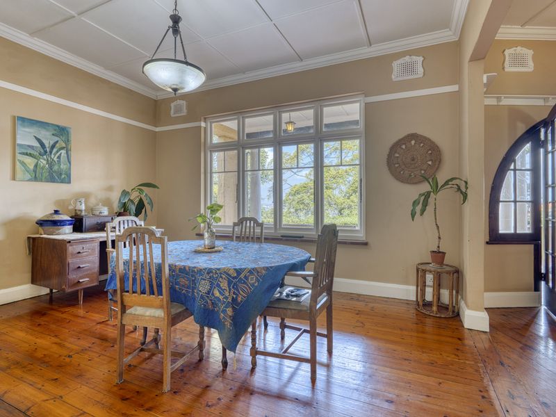 A dining room featuring polished timber flooring, classic picture rails, and large windows that provide natural light and garden views.