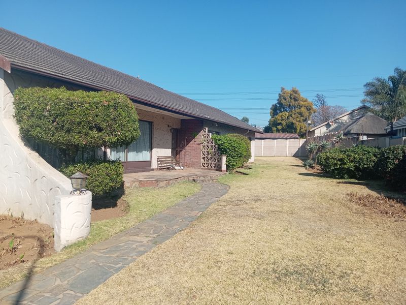 Rear view of the house featuring a stone pathway, established garden, and a covered patio area with brick accents.