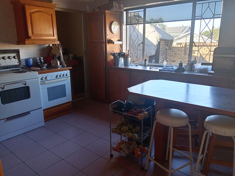 A functional kitchen featuring wooden cabinetry, tiled flooring, a freestanding stove, and a built-in breakfast counter with natural light from a large window.