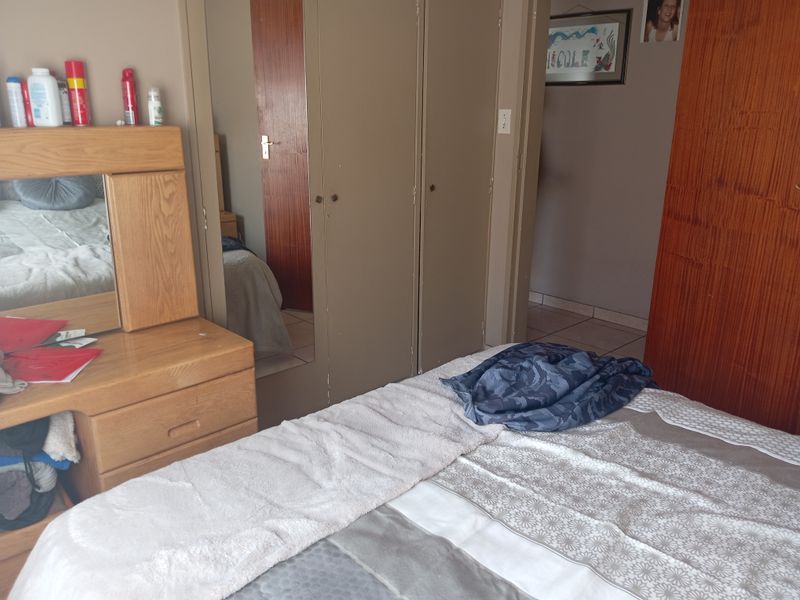 Bedroom featuring built-in cupboards with mirrored doors and tiled flooring, offering functional storage space in a dated interior setting.
