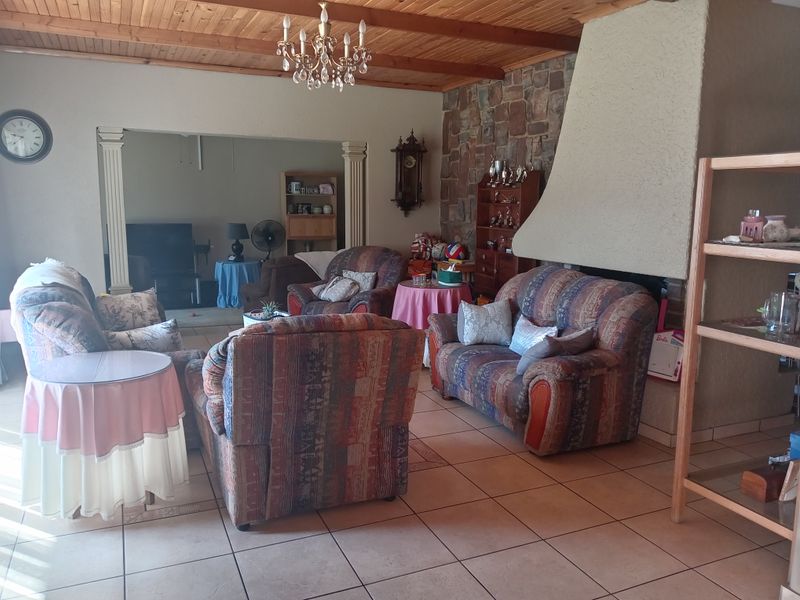 Spacious living room featuring a stone fireplace, exposed timber ceiling, and ceramic floor tiles, offering a traditional aesthetic with potential for modern updates.