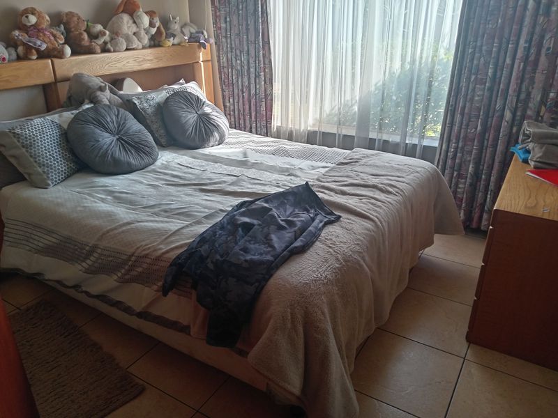 A bedroom featuring tiled flooring and a built-in wooden headboard, with large windows allowing for natural light.