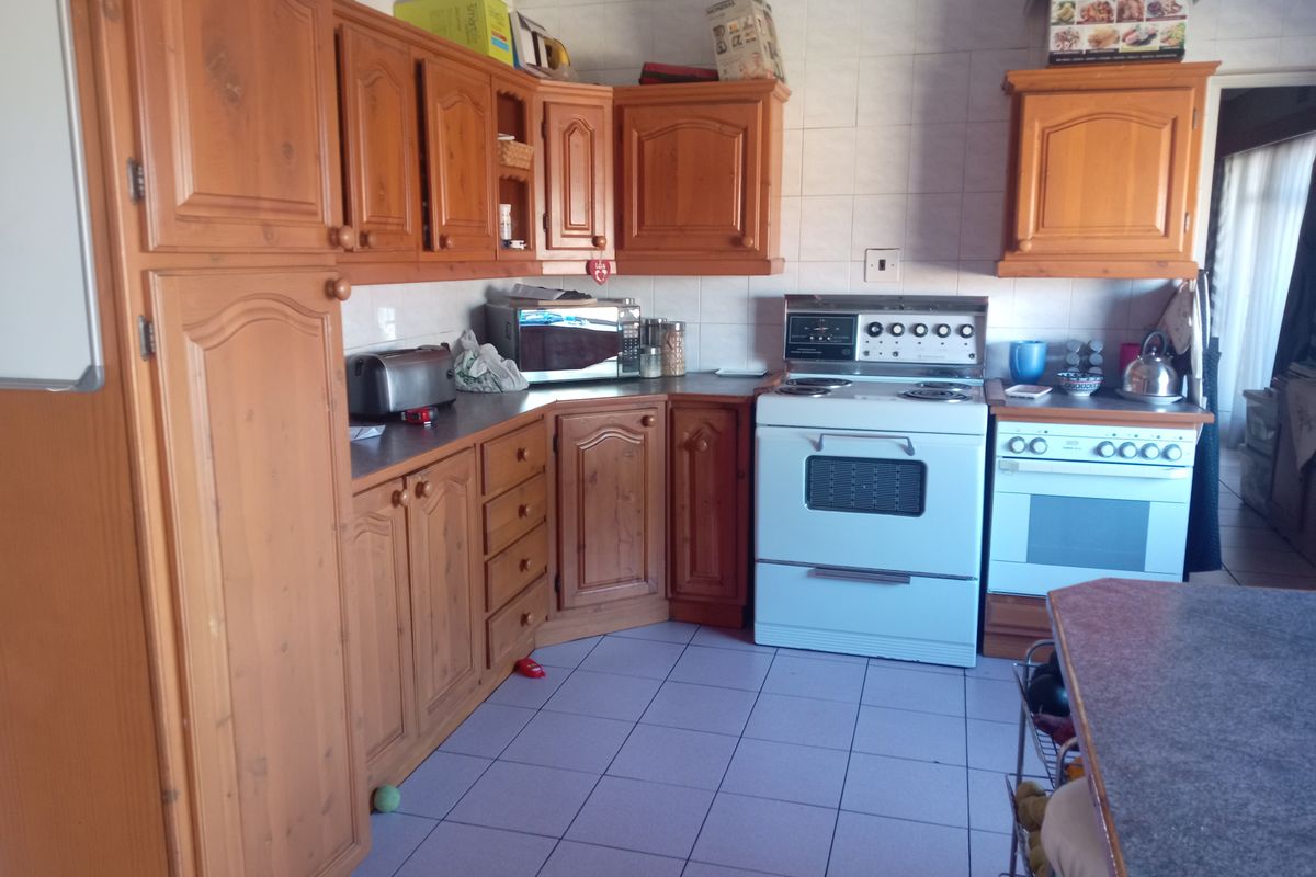 A dated kitchen featuring traditional wooden cabinetry, tiled flooring, and a freestanding stove, offering significant potential for a modern renovation.