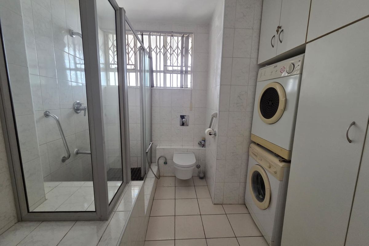 A functional bathroom featuring a walk-in shower, wall-mounted toilet, and integrated laundry cabinetry with stacked appliances.