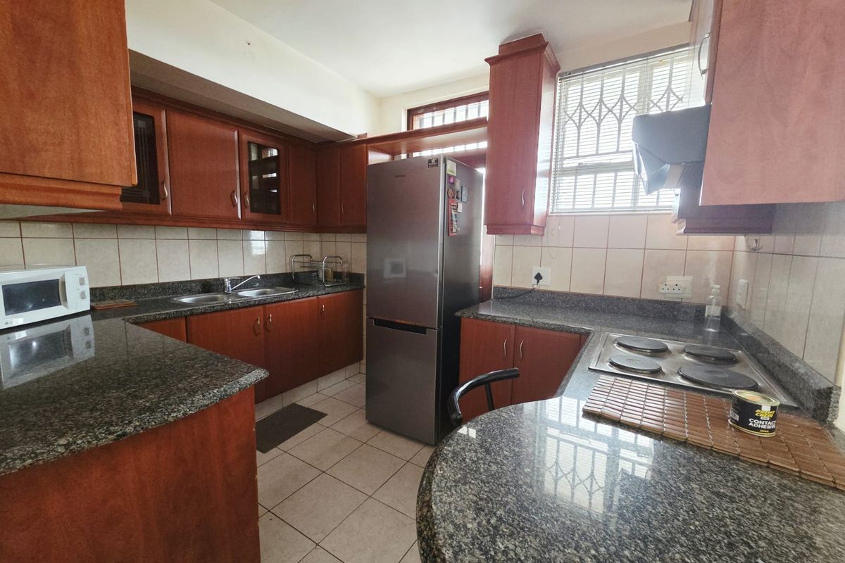 A functional kitchen featuring granite countertops, wooden cabinetry, tiled backsplash, and an integrated electric hob with extractor fan.