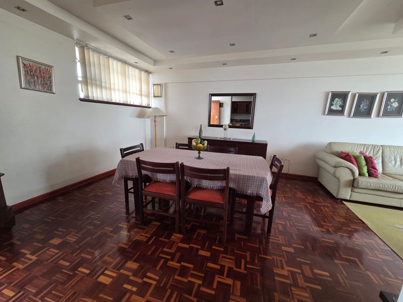Spacious living and dining area featuring classic parquet flooring, recessed ceiling lighting, and large windows with vertical blinds.