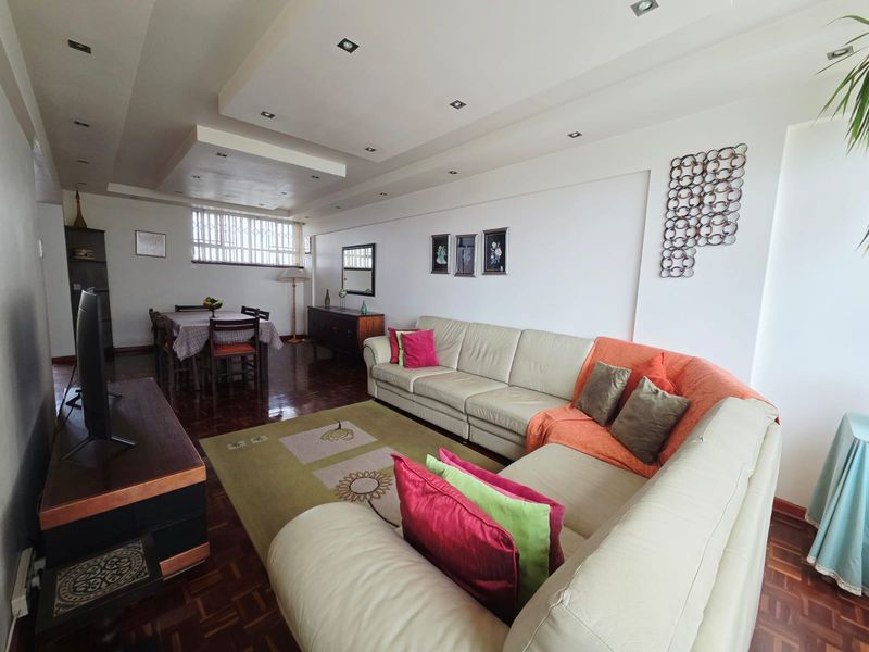 Spacious open-plan living and dining area featuring parquet flooring, recessed ceiling lighting, and a window with security bars.