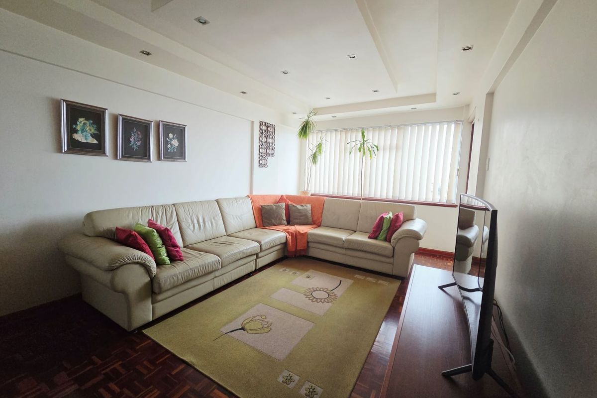 A well-lit living room featuring parquet flooring, recessed ceiling lighting, and large windows with vertical blinds.