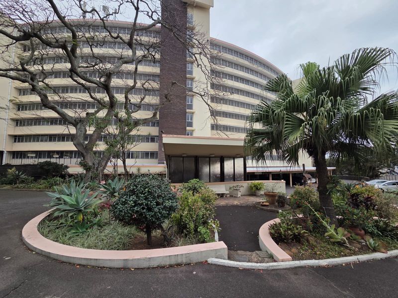 Exterior view of a multi-story apartment building featuring a landscaped garden area and a covered entrance canopy.