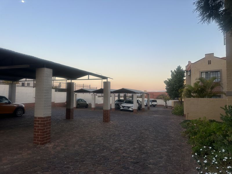 A well-maintained outdoor parking area featuring multiple covered bays with brick pillars and paved surfacing within an apartment complex.