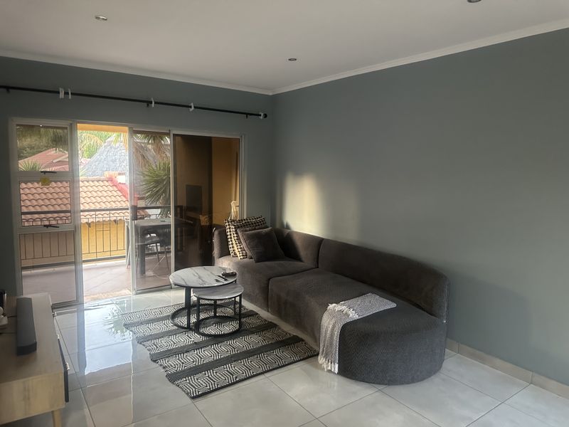 A bright living room featuring tiled flooring, recessed downlights, and a large sliding glass door providing access to an outdoor balcony area.