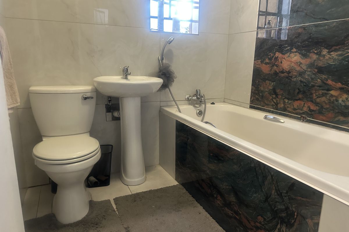 A functional bathroom featuring a pedestal basin, toilet, and a bathtub with decorative stone-look tiling.