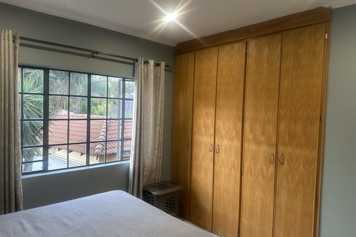 A bedroom featuring a large built-in wooden wardrobe and a steel-framed window overlooking the exterior.