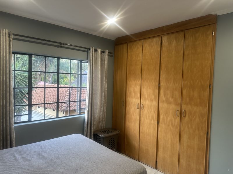 A bedroom featuring a large built-in wooden wardrobe and a steel-framed window overlooking the exterior.