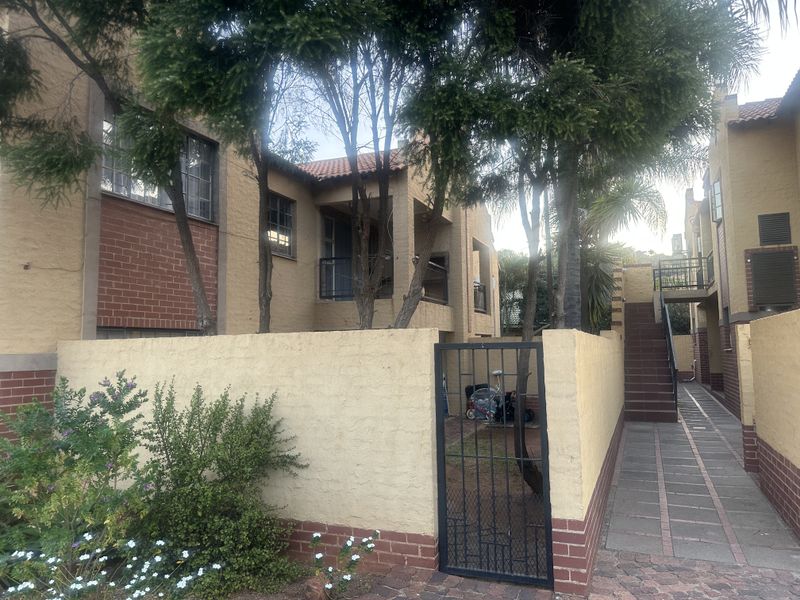 Exterior view of an apartment complex featuring a gated entrance, paved walkway, staircase, and balcony with a traditional brick and plaster facade.