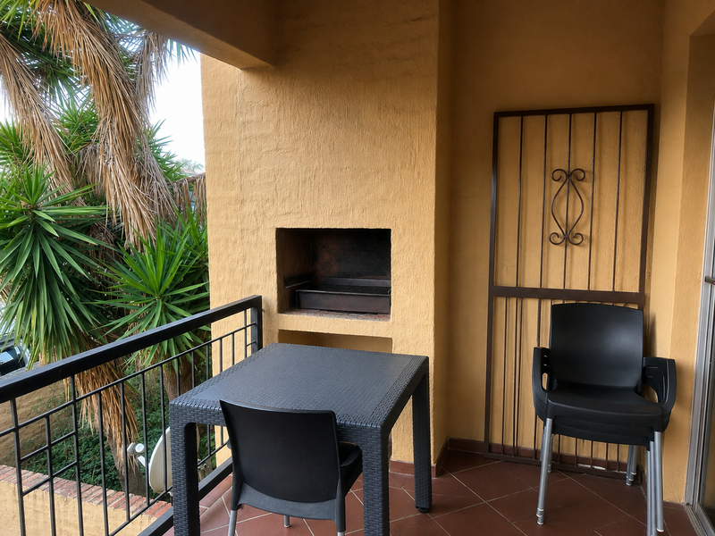 Covered balcony featuring a built-in braai, tiled flooring, and a metal balustrade, providing an outdoor entertainment space.