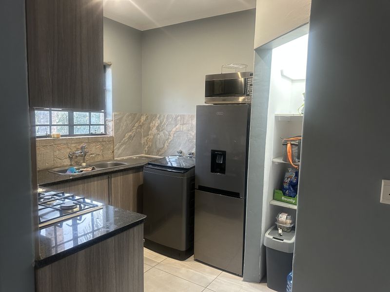 Compact kitchen featuring modern wood-finish cabinetry, granite countertops, a gas hob, and a stone tile backsplash with integrated shelving.
