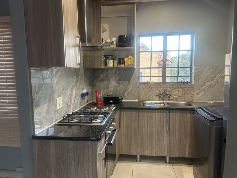Compact kitchen featuring wood-finish cabinetry, granite countertops, gas hob, extractor fan, and marble-look splashback tiles, with some minor finishing work required around the window.