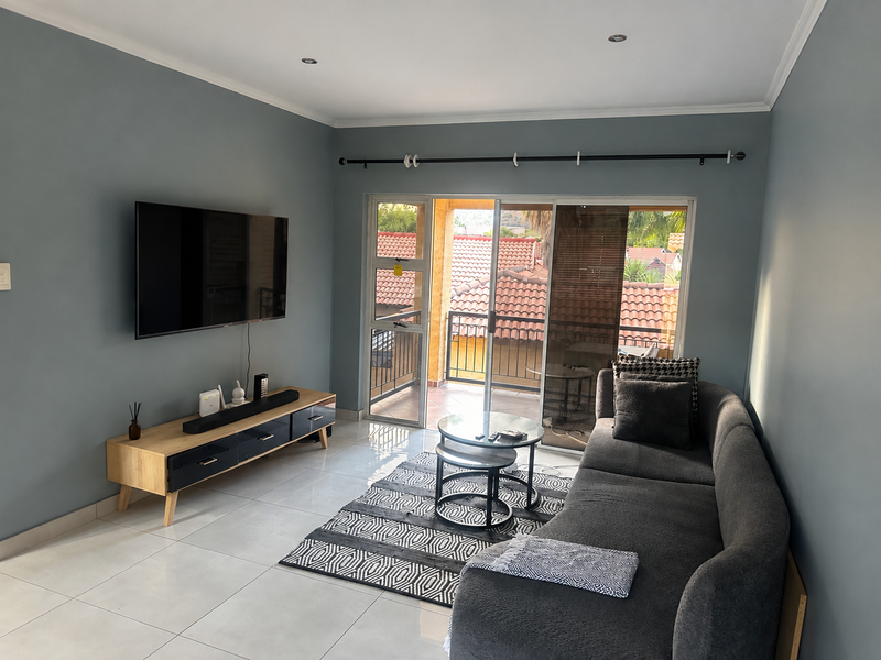 A well-maintained living room featuring tiled flooring, recessed lighting, and a sliding glass door providing direct access to a private balcony.
