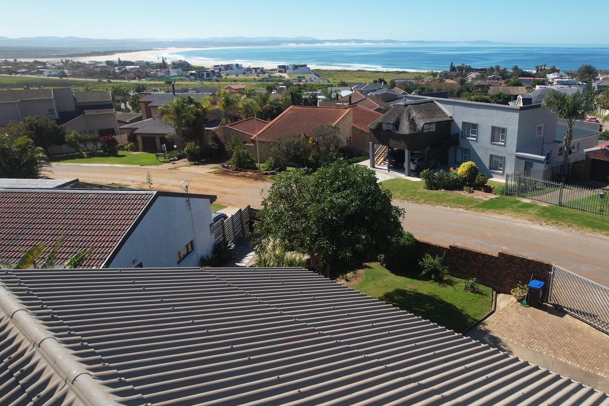 Aerial view of the property showing the roof structure, driveway, and surrounding residential neighborhood with a distant coastal view.