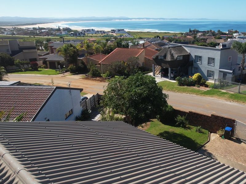 Aerial view of the property showing the roof structure, driveway, and surrounding residential neighborhood with a distant coastal view.