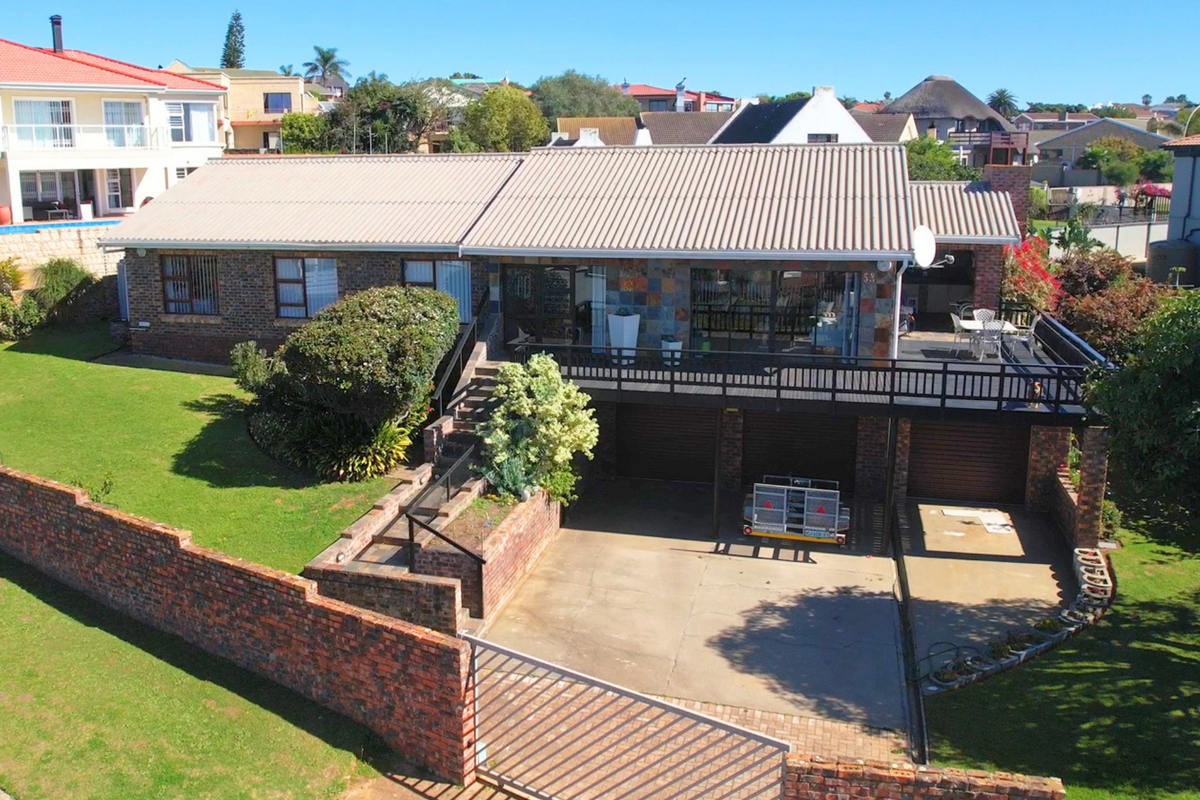 Aerial view of a brick-faced house featuring a raised timber deck, double garage, concrete driveway, and a well-maintained garden with perimeter brick walling.