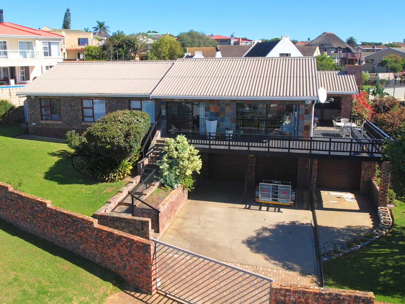 Aerial view of a brick-faced house featuring a raised timber deck, double garage, concrete driveway, and a well-maintained garden with perimeter brick walling.
