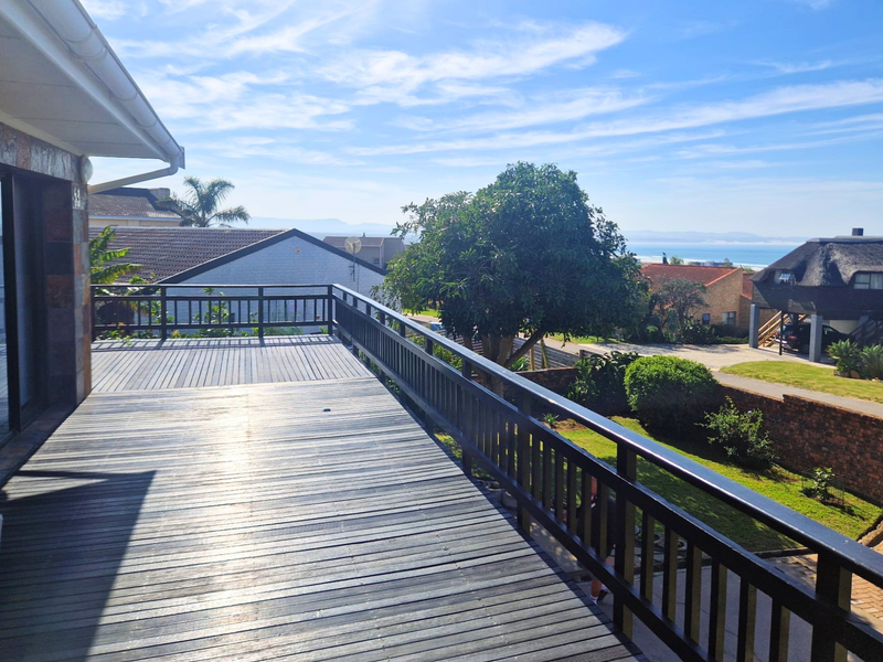 Spacious elevated timber deck balcony featuring a railing and sliding glass door access, offering pleasant neighbourhood and distant coastal views.