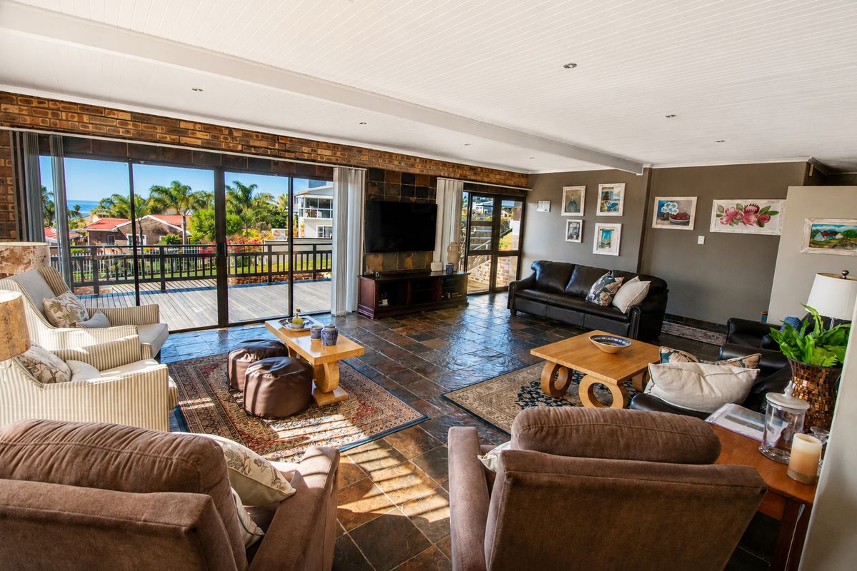 Spacious living room featuring slate tile flooring, exposed brick accents, and large sliding glass doors opening onto a timber deck with scenic views.