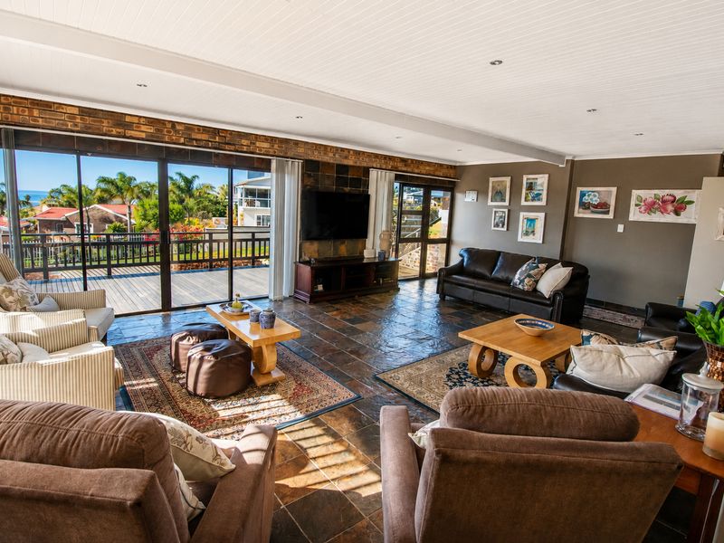 Spacious living room featuring slate tile flooring, exposed brick accents, and large sliding glass doors opening onto a timber deck with scenic views.