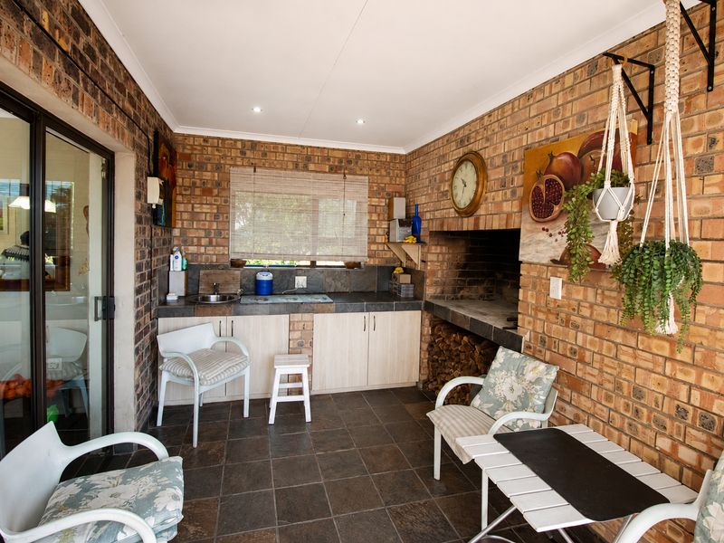 Covered patio area featuring a built-in braai, brick wall finishes, tiled flooring, and a convenient kitchenette with sink and storage cabinetry.