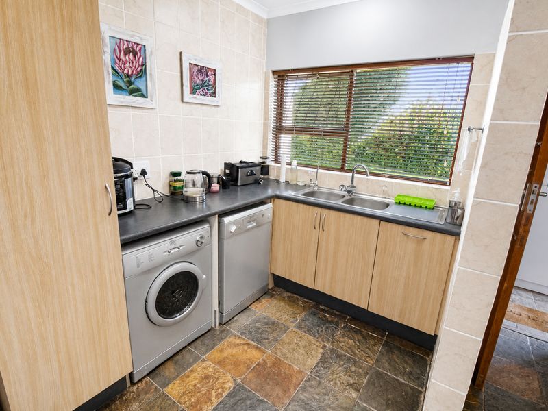 Functional scullery area featuring laminate cabinetry, double basin sink, tiled backsplash, and slate flooring, providing convenient space for laundry and wash-up tasks.