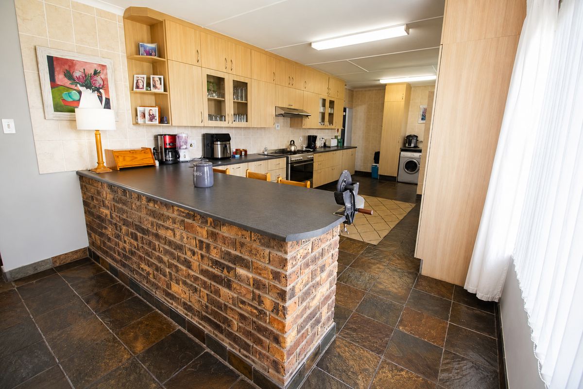 Spacious kitchen featuring a brick breakfast bar, extensive laminate cabinetry, built-in oven and hob, and durable slate tile flooring.
