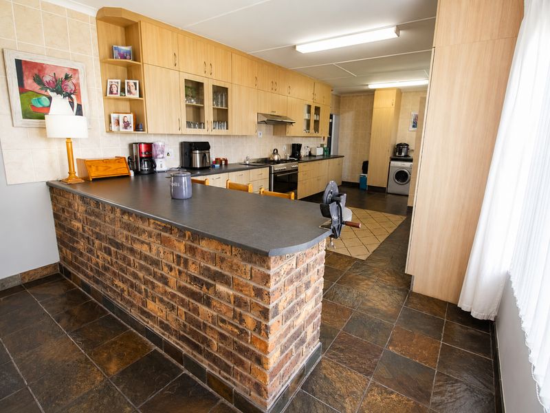 Spacious kitchen featuring a brick breakfast bar, extensive laminate cabinetry, built-in oven and hob, and durable slate tile flooring.