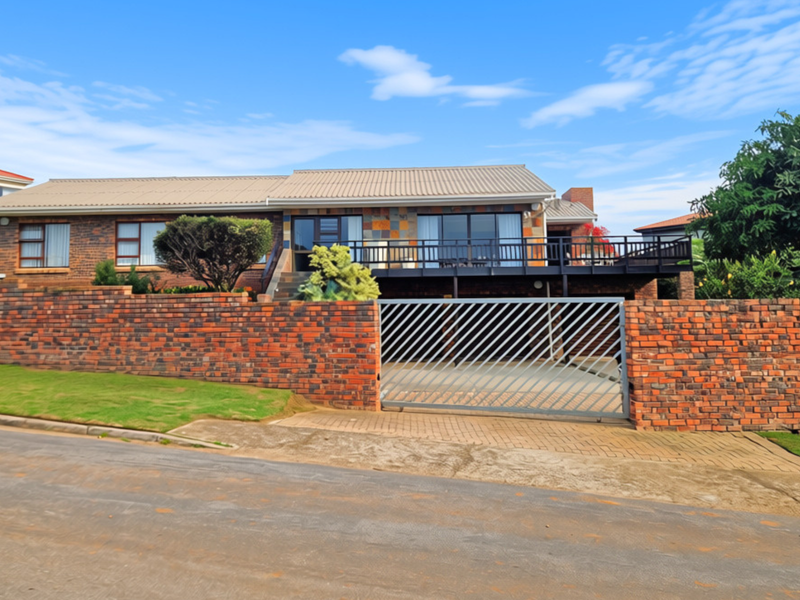 Front elevation of a facebrick house featuring a raised timber deck, paved driveway, and secure gated entrance with a brick boundary wall.