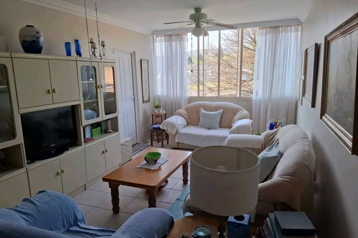 A comfortable living room featuring tiled flooring, a ceiling fan, and a large window that allows for natural light.