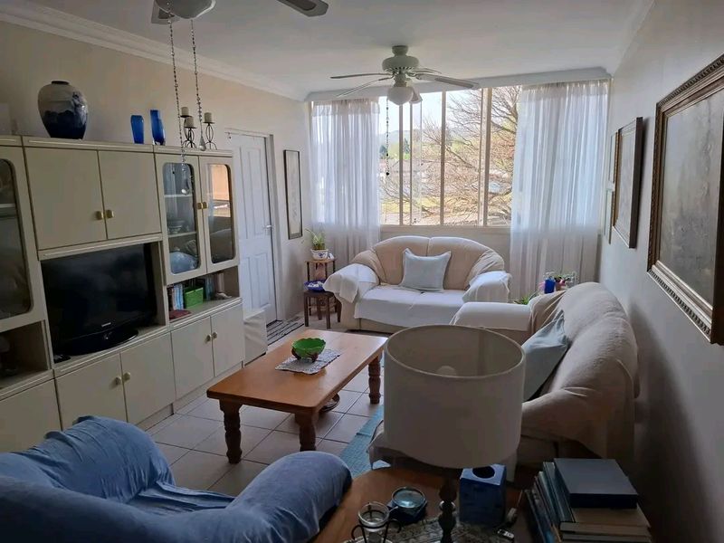 A comfortable living room featuring tiled flooring, a ceiling fan, and a large window that allows for natural light.