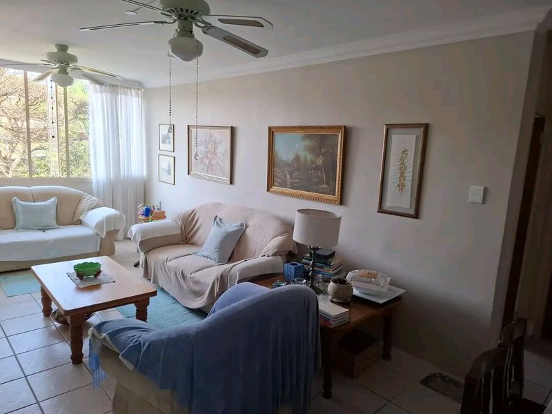 A comfortable living room featuring tiled flooring, ceiling fans, and large windows that provide ample natural light.