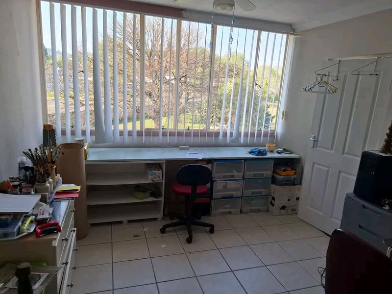A functional office space featuring tiled flooring, a built-in desk area, and large windows with vertical blinds, offering natural light and exterior views.