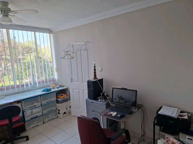 A functional office space featuring tiled flooring, a ceiling fan, and large windows with vertical blinds, offering potential for a modern workspace renovation.